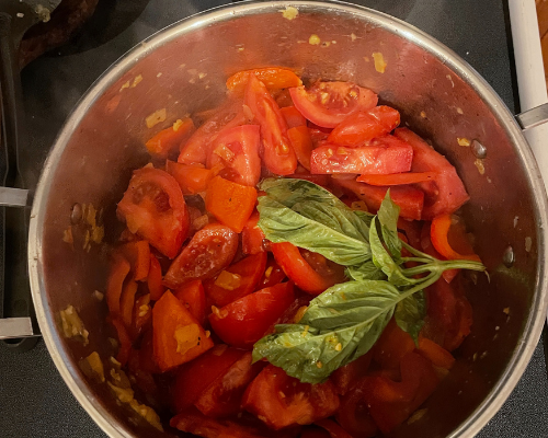 Tomatoes and basil are added to a pot on the stove 